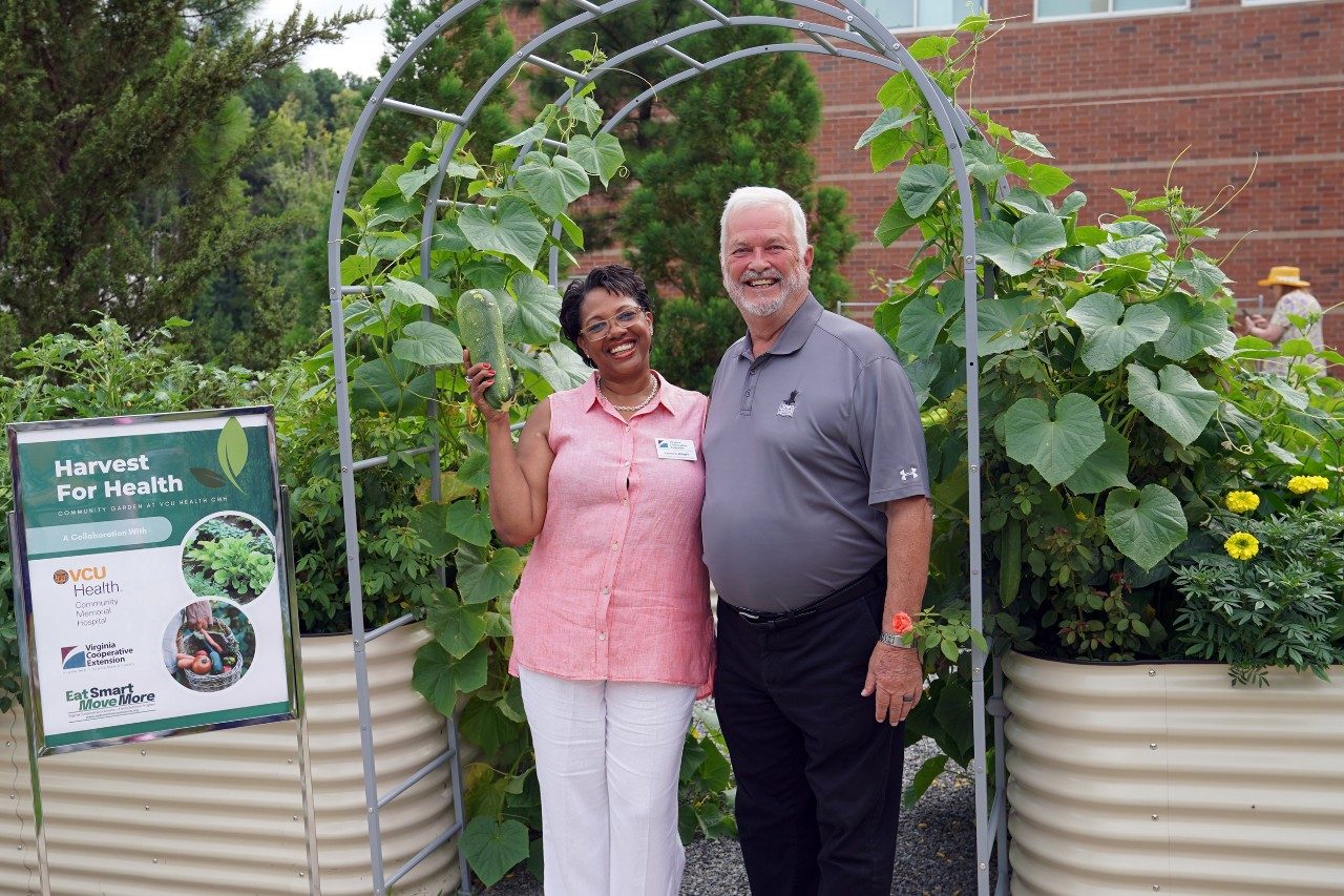 two people smiling under an arbor holding vegetables