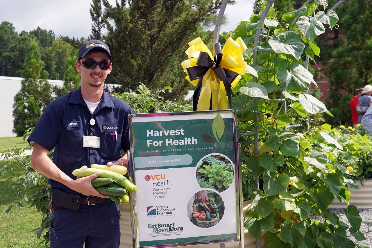 person standing by Harvest for Health sign holding cucumbers